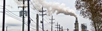 Electrical poles and wires with smokestacks blowing smoke in the background