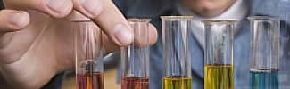 A scientist's hand reaching out to touch various test tubes filled with different colored liquids